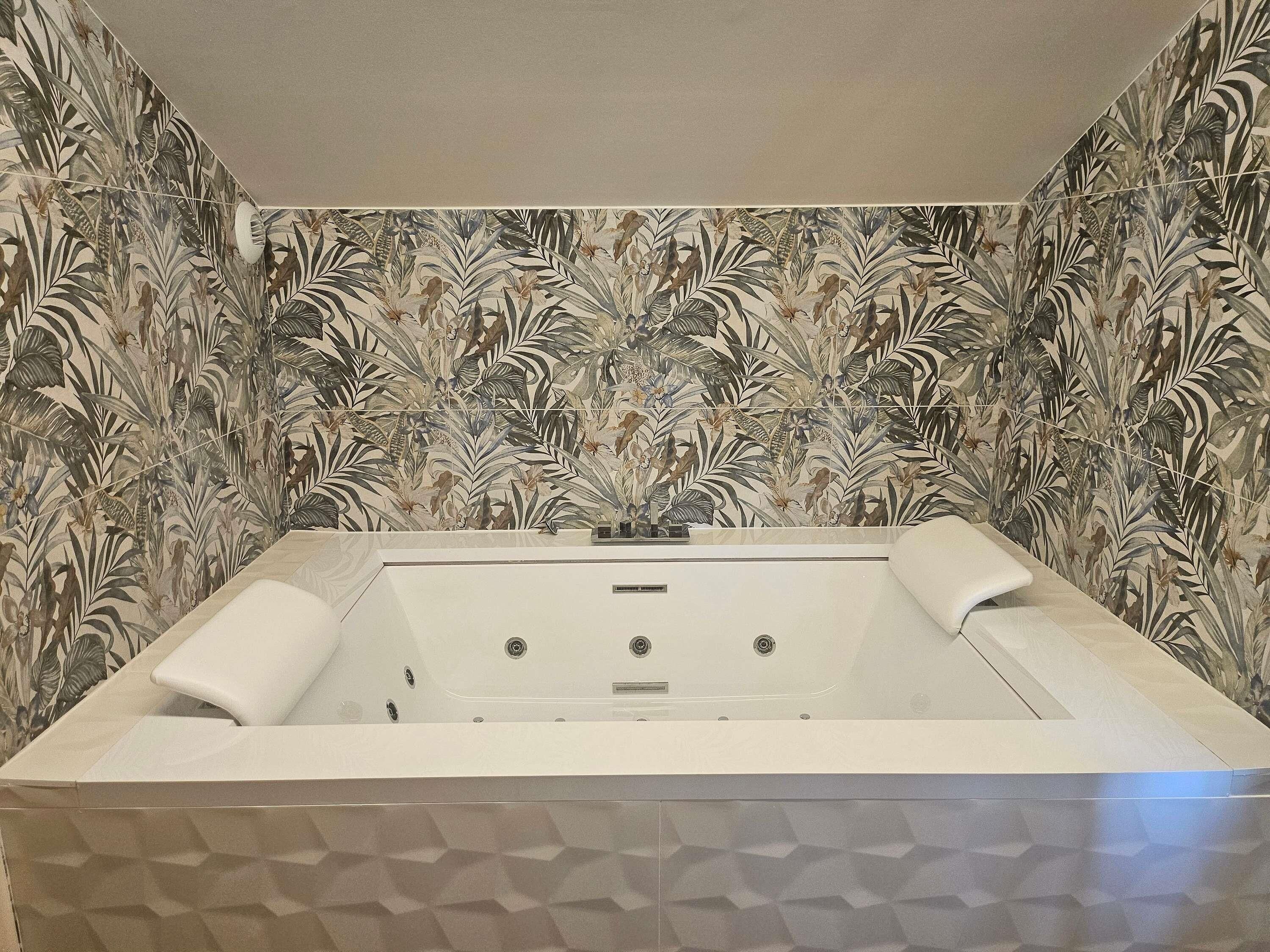 Un bagno con una vasca da bagno ampia, una doccia e una parete decorata con un motivo a foglia.