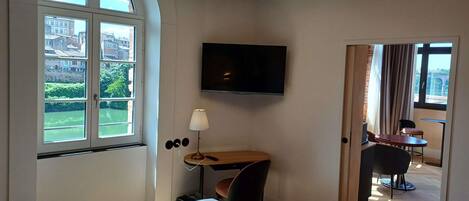 Habitación de hotel con cama, escritorio, televisión y vistas a la ciudad a través de amplias ventanas.