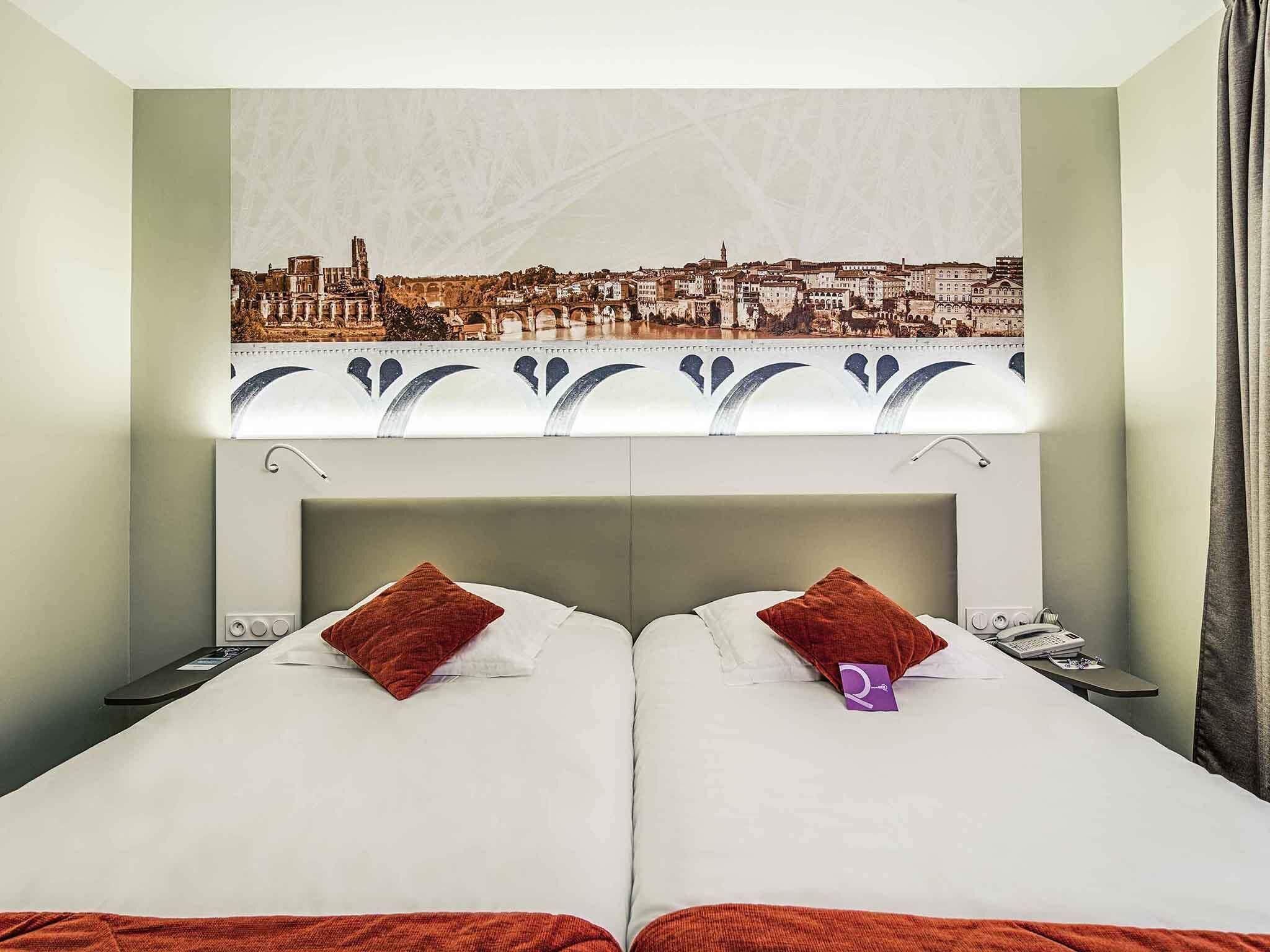 A hotel room with two beds, a cityscape view, a patterned headboard, and a bedside table with a phone.