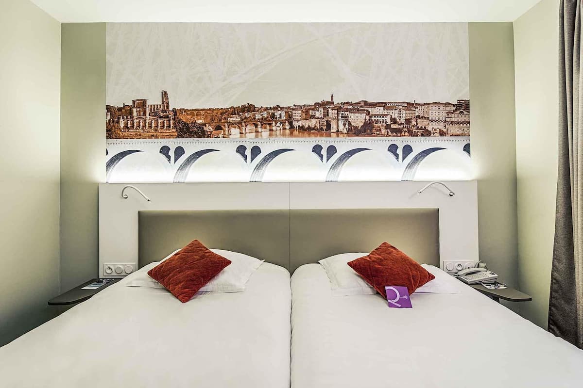 A hotel room with two beds, a cityscape view, a patterned headboard, and a bedside table with a phone.