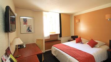 Habitación de hotel con cama, escritorio, silla, lámpara y televisor montado en la pared.