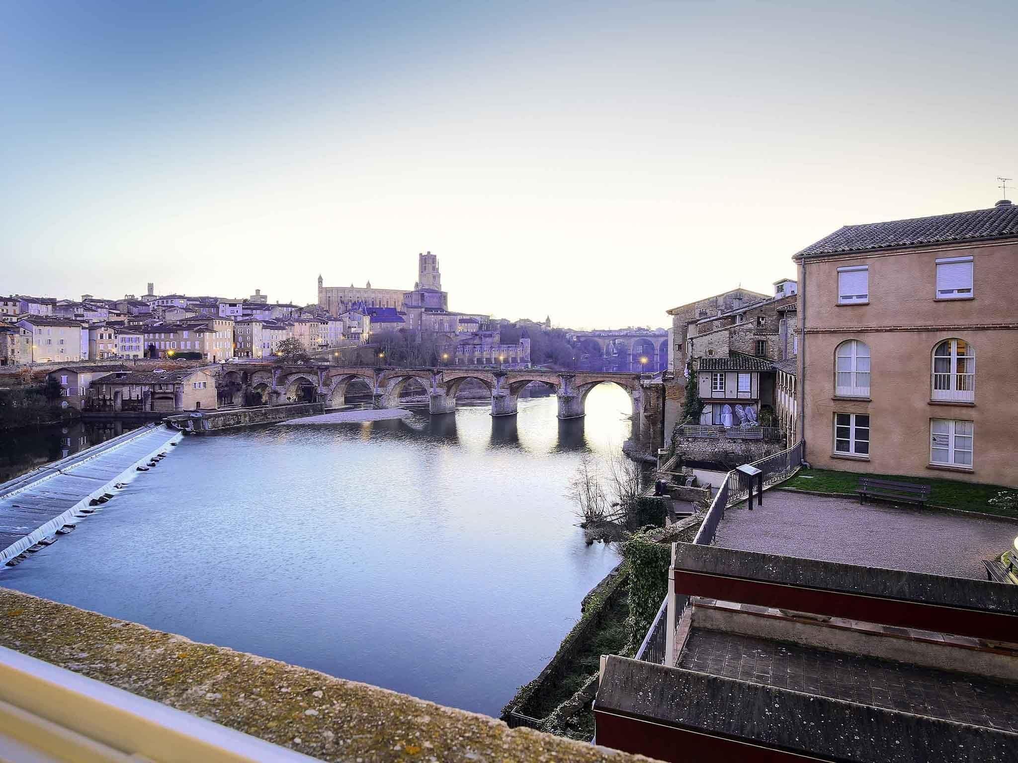 Ein Fluss mit einer Steinsbrücke, Häuser an beiden Seiten und ein weiter Turm in der Ferne.
