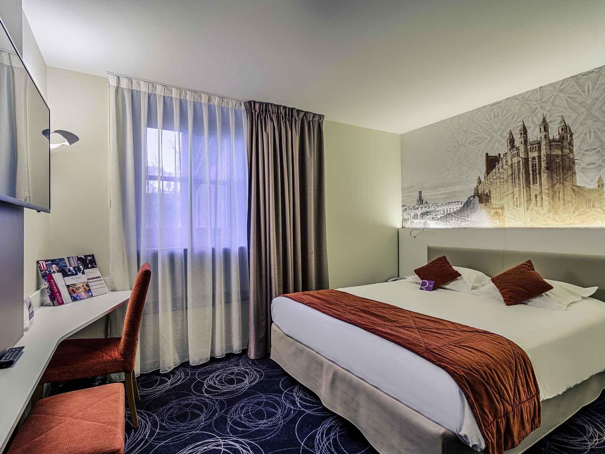 A hotel room with a bed, a desk, a chair, a TV, and a large window with curtains.