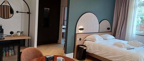 A hotel room with a bed, a desk, a chair, a coffee table, and a trash bin.