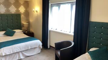 A hotel room with two beds, a chair, a nightstand, a lamp, and a window with curtains.