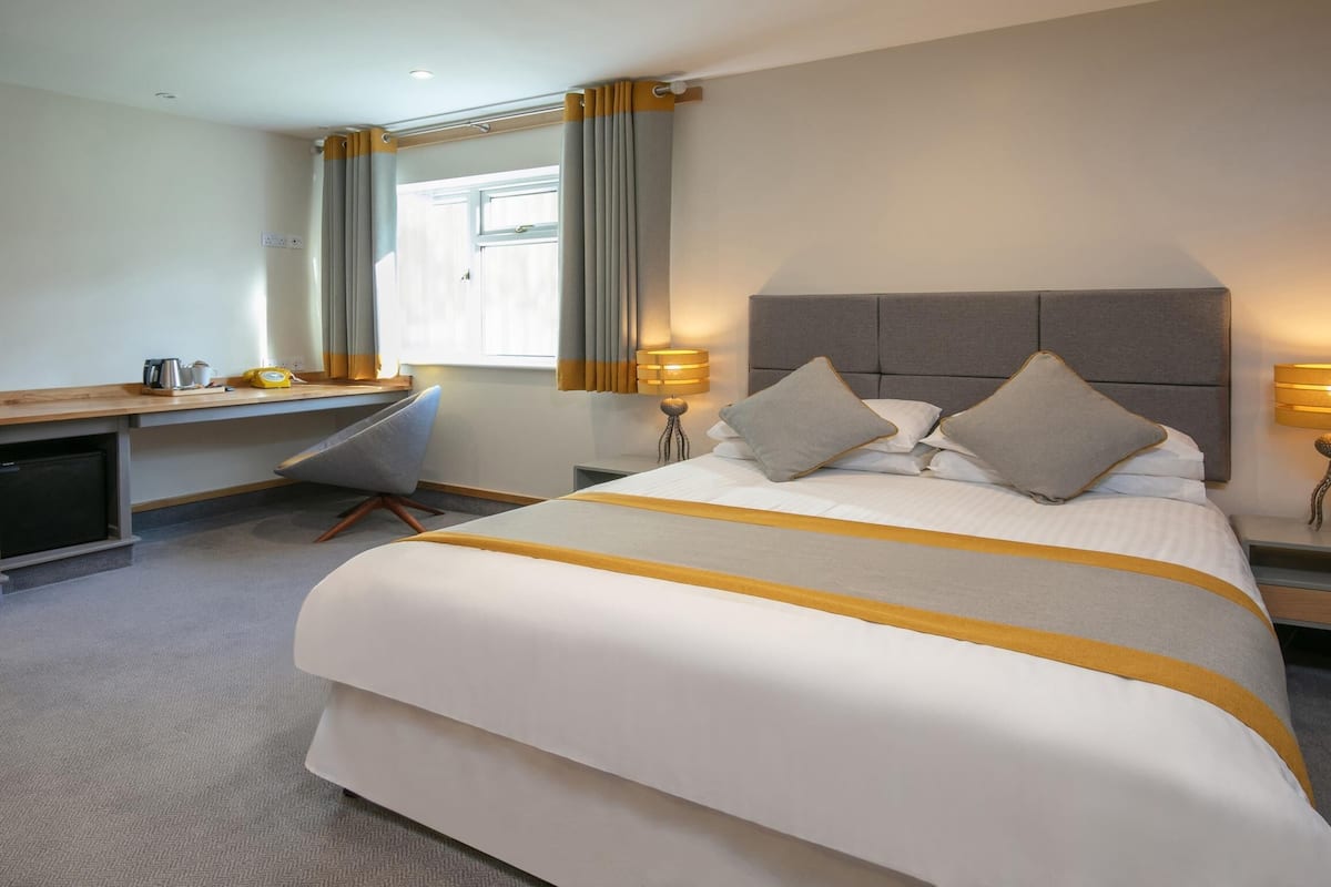 A hotel room with a large bed, a desk, a mirror, and two bedside lamps.