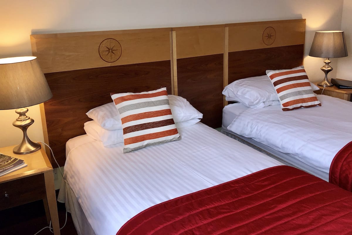 Two beds with striped pillows, a wooden headboard, and bedside lamps.