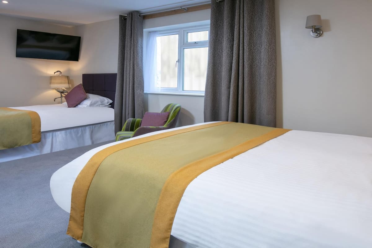A hotel room with two beds, a TV mounted on the wall, a window with curtains, and a lamp on the nightstand.
