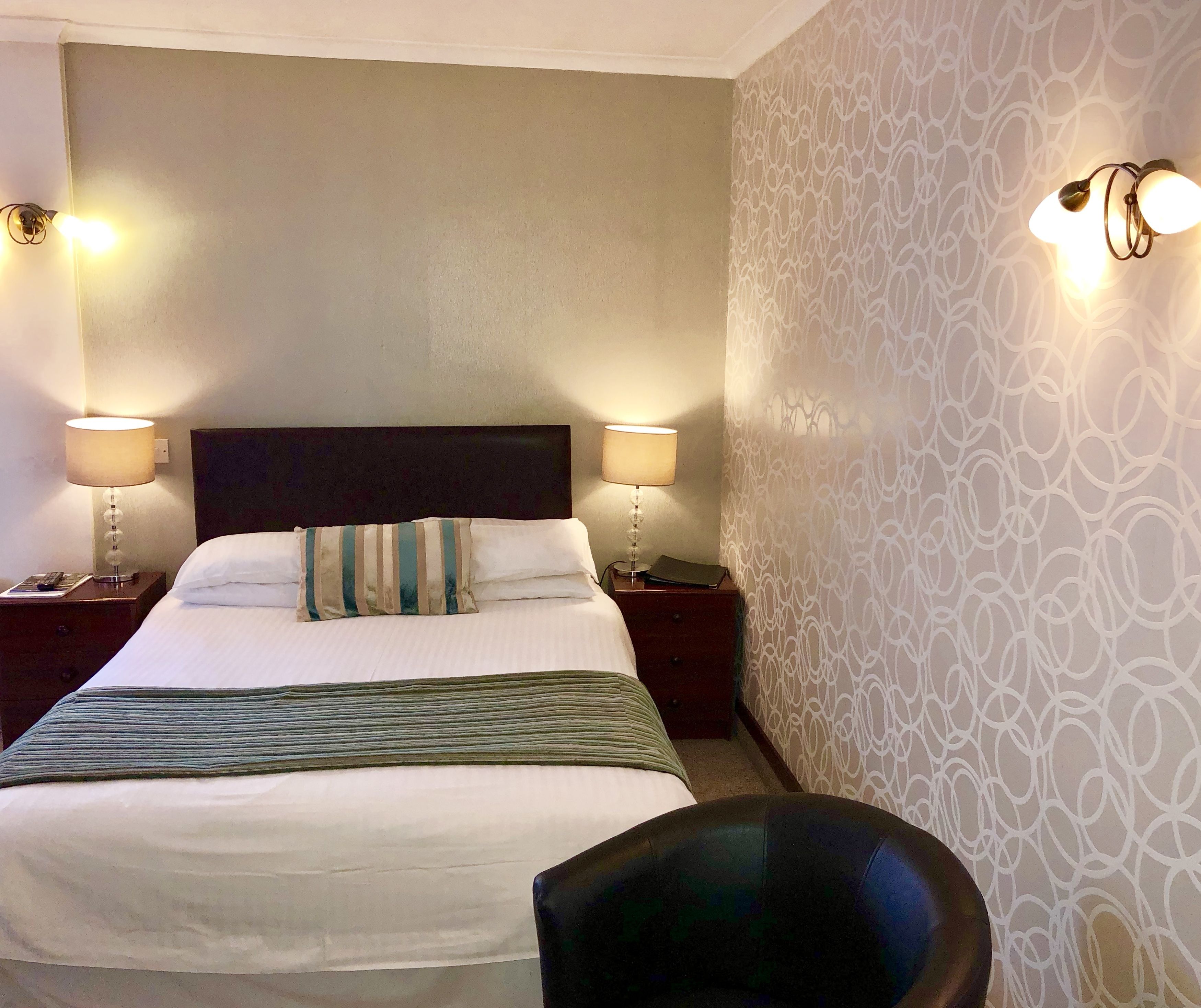 Habitación de hotel con una cama grande, dos lámparas de noche, un papel tapiz decorado y una silla.