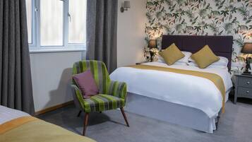 A hotel room with a large bed, a striped armchair, a nightstand, and a window with curtains.