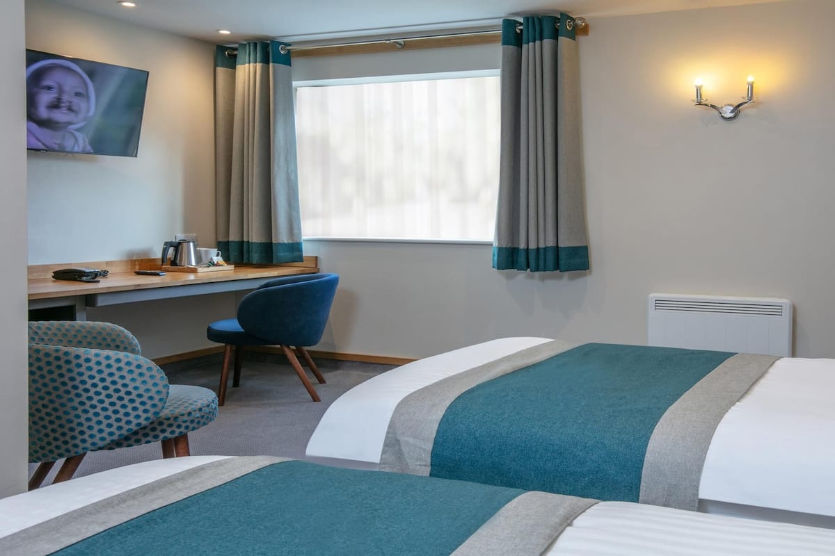 A hotel room with two beds, a desk with a chair, a TV, and a window with curtains.