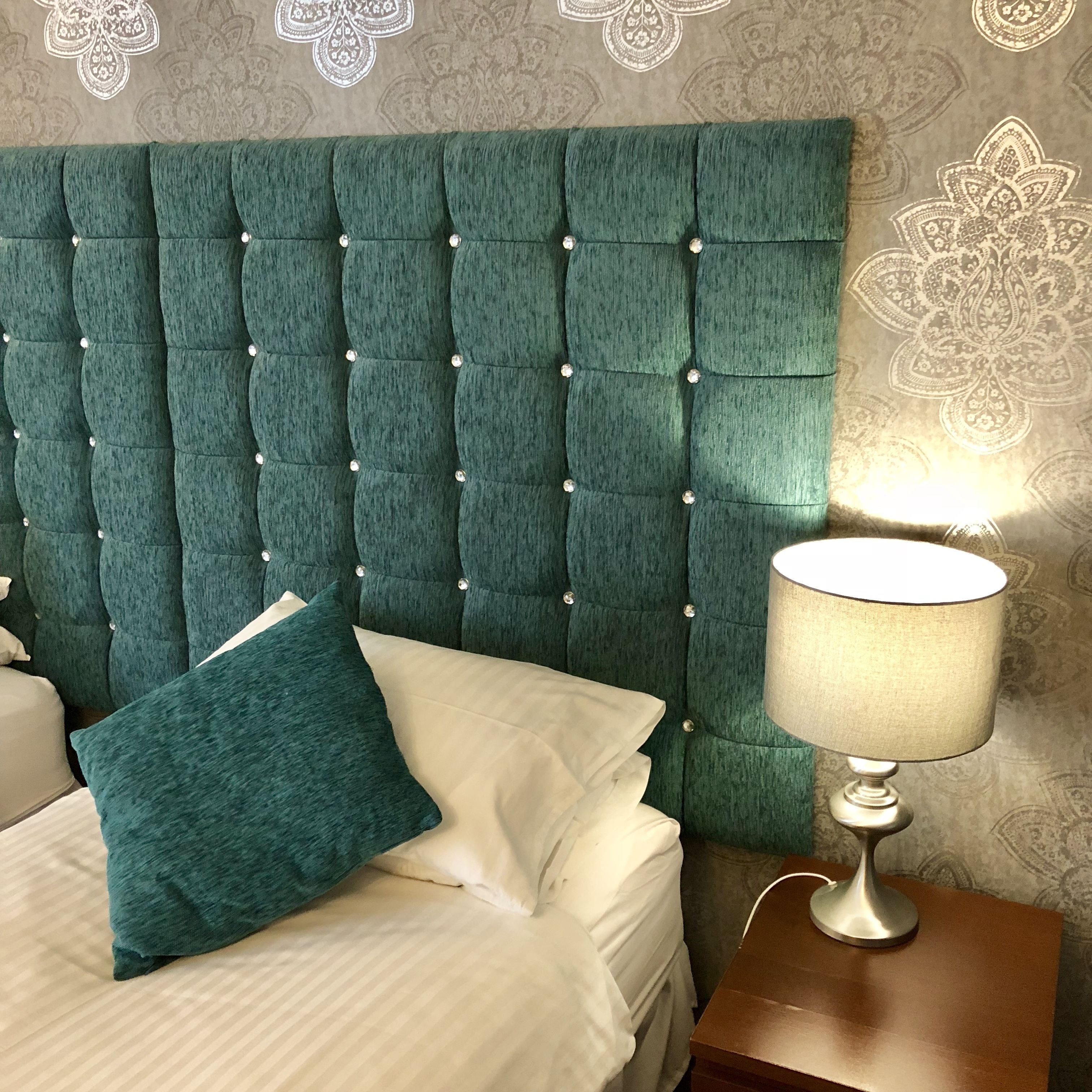 A bed with a teal upholstered headboard, a white pillow, and a bedside lamp.