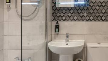 A modern bathroom with a glass-enclosed shower, a pedestal sink, and a toilet.