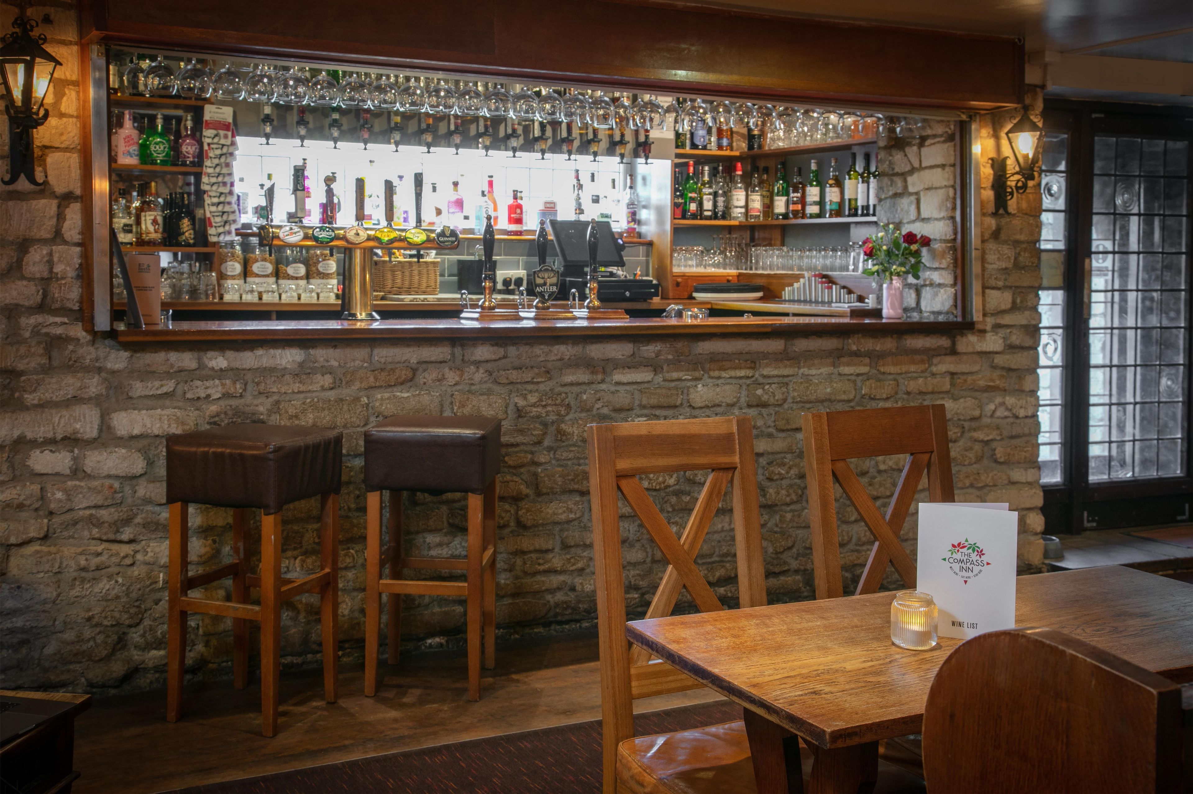 Uma área de bar com banquetas, uma mesa de madeira e um letreiro com a carta de vinhos.