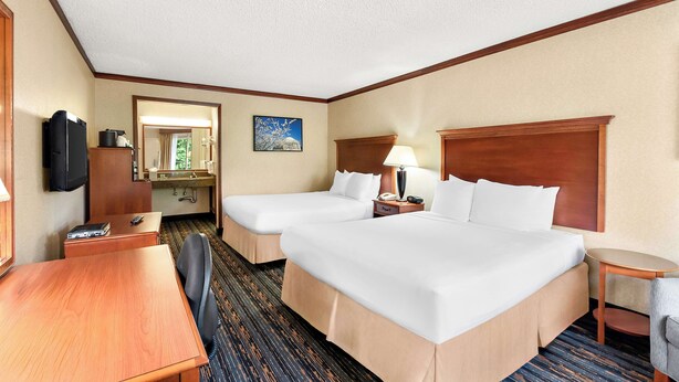 A hotel room with two beds, a desk, a chair, a small table, a lamp, a TV, and a bathroom visible through an open door. - Best Western Fairfax (Fairfax)