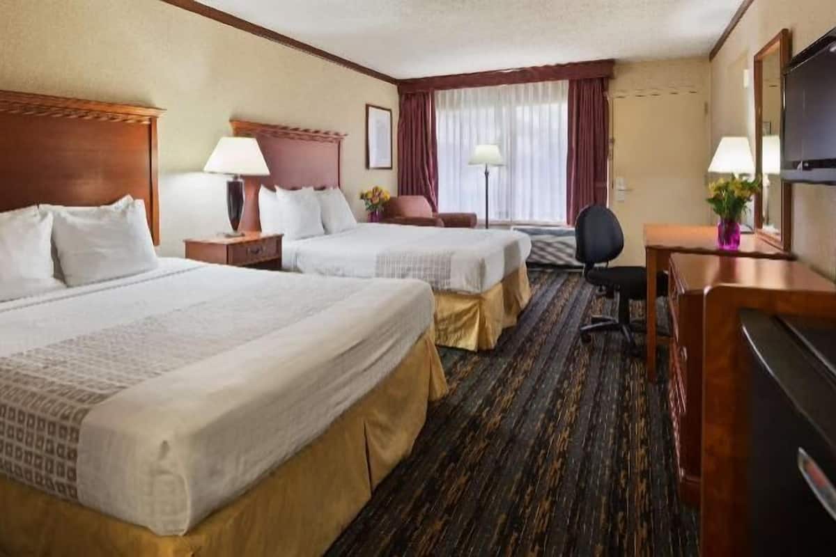 A hotel room with two beds, a desk, a chair, a TV, and a window with curtains.