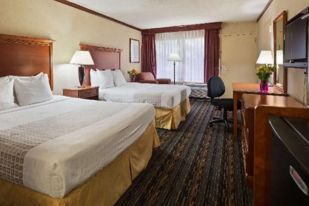 A hotel room with two beds, a desk, a chair, a TV, and a window with curtains.