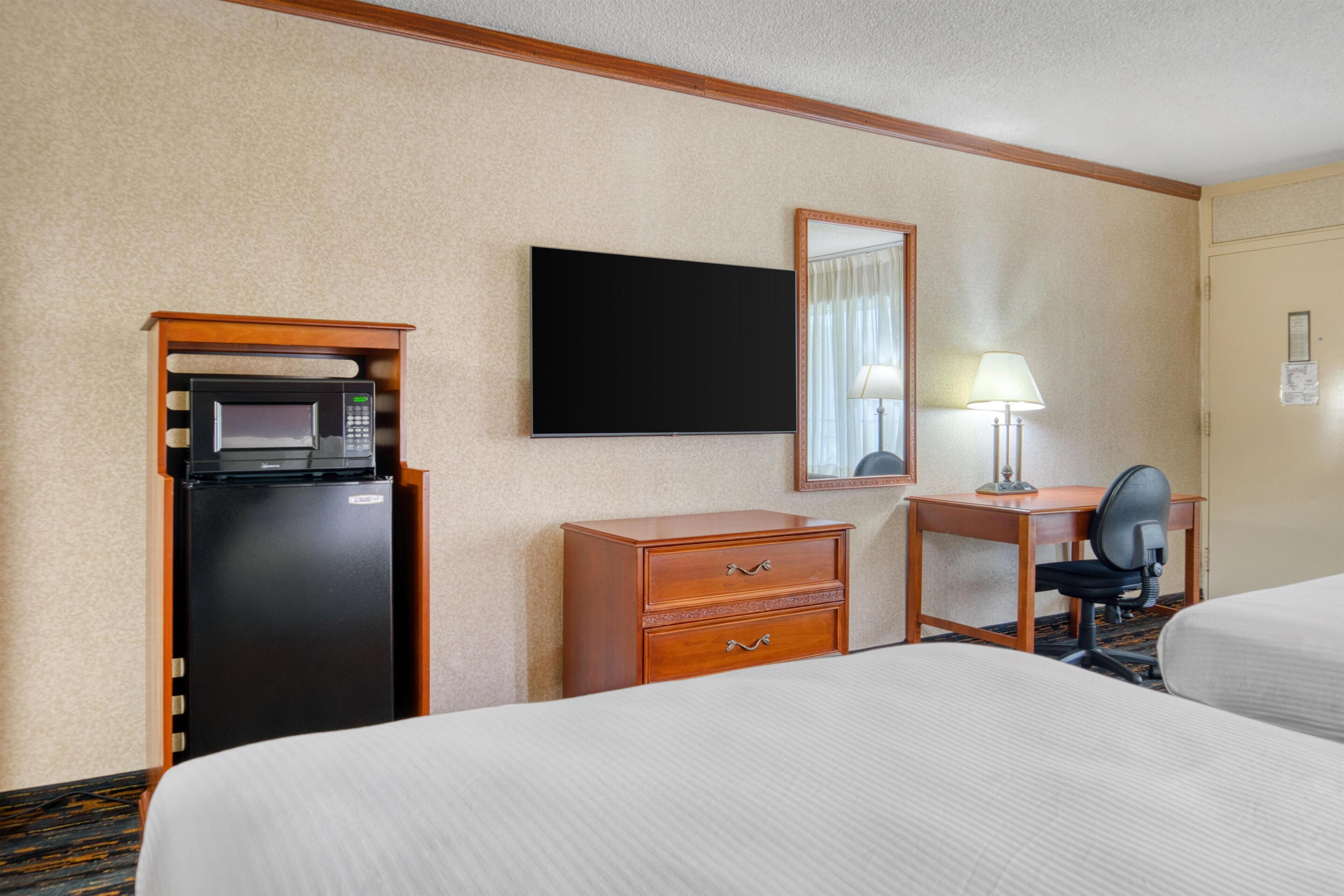 Une chambre d’hôtel équipée d’un lit, d’un bureau, d’une chaise, d’une télévision, d’un four à micro-ondes et d’un réfrigérateur.