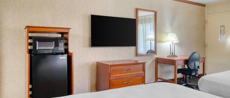 Une chambre d’hôtel équipée d’un lit, d’un bureau, d’une chaise, d’une télévision, d’un four à micro-ondes et d’un réfrigérateur.
