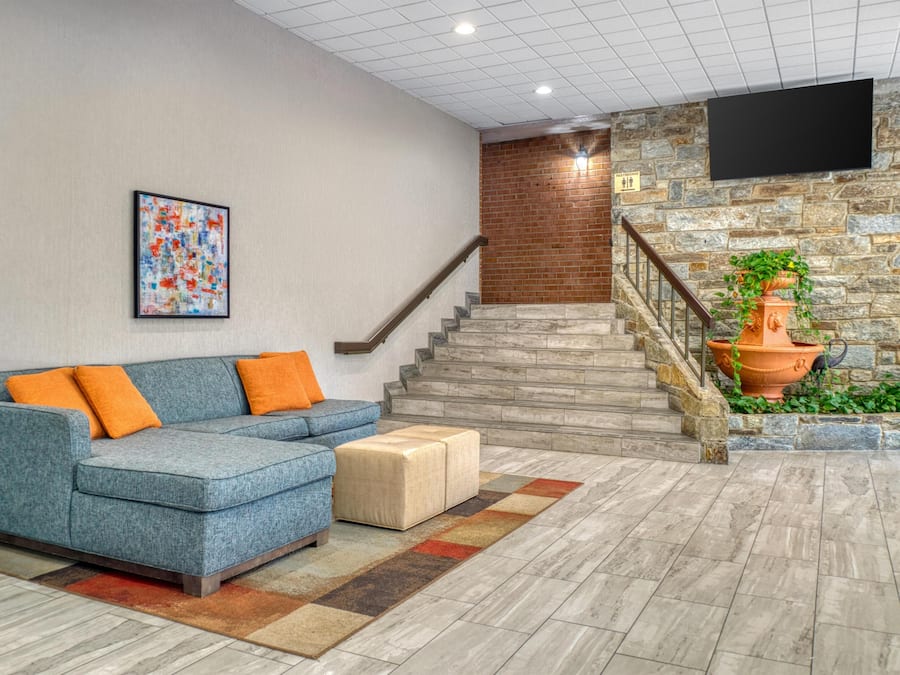 A modern lobby with a blue sofa, a staircase, and a flat-screen TV mounted on the wall.