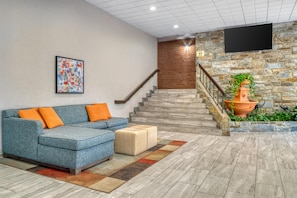 A modern lobby with a blue sofa, a staircase, and a flat-screen TV mounted on the wall.