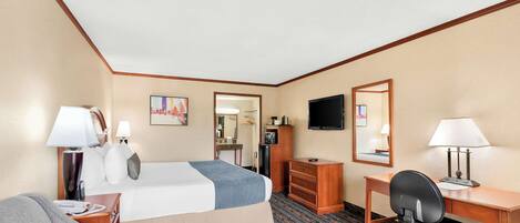 A hotel room with a bed, a desk, a chair, a television, and a desk lamp.