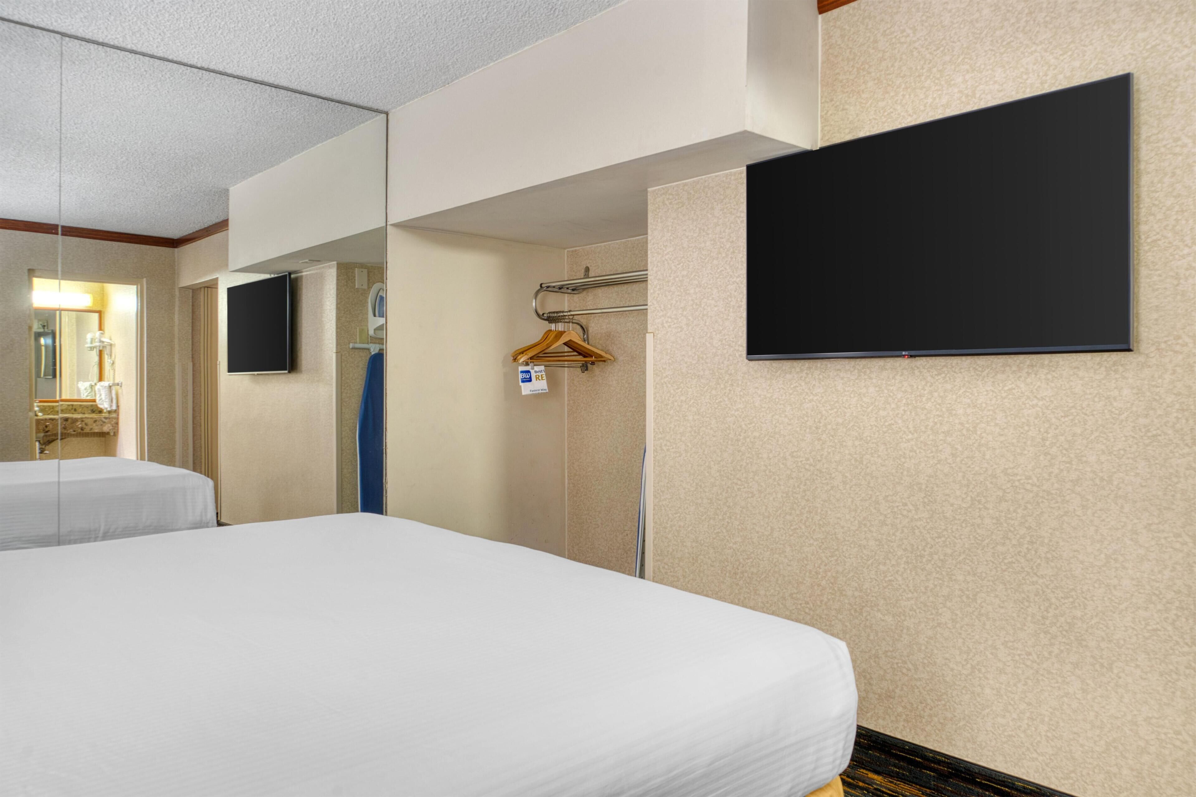 A hotel room with two beds, a flat-screen TV, a towel rack, and a shower area.