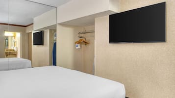 A hotel room with two beds, a flat-screen TV, a towel rack, and a shower area.