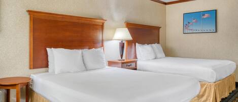 A hotel room with two beds, a nightstand with a lamp, and a framed picture of flags on the wall.