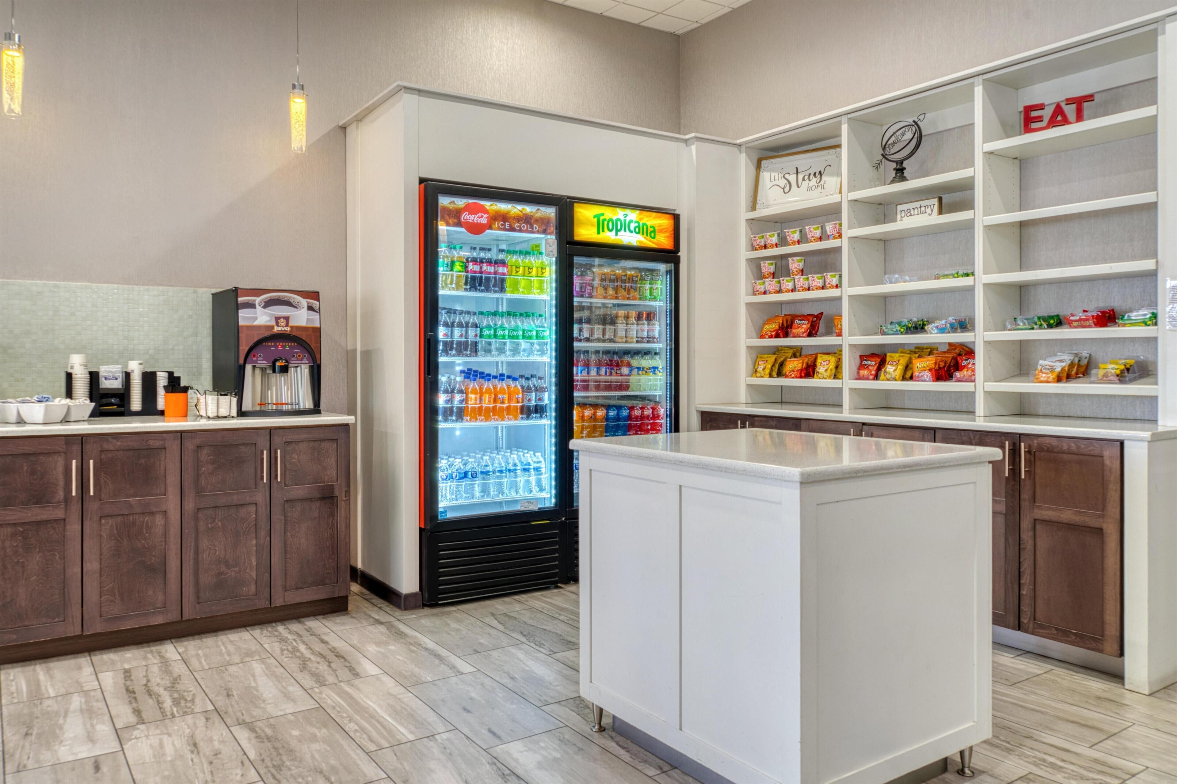 A kitchenette area with a refrigerator stocked with beverages, a coffee machine, and a pantry shelf with snacks.