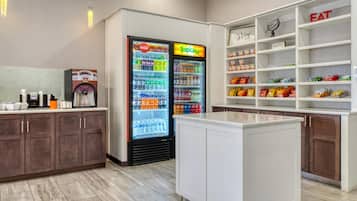 A kitchenette area with a refrigerator stocked with beverages, a coffee machine, and a pantry shelf with snacks.