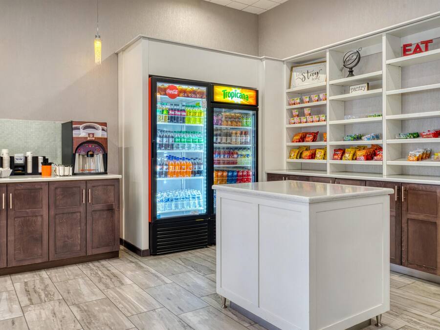 A kitchenette area with a refrigerator stocked with beverages, a coffee machine, and a pantry shelf with snacks.