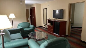 A hotel room with a green sofa set, a glass coffee table, a TV on a wooden cabinet, and a lamp. - Ramada by Wyndham Rochelle Park Near Paramus (Rochelle Park)