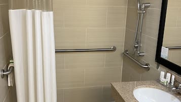 A bathroom with a shower, grab bars, a sink, and a mirror.