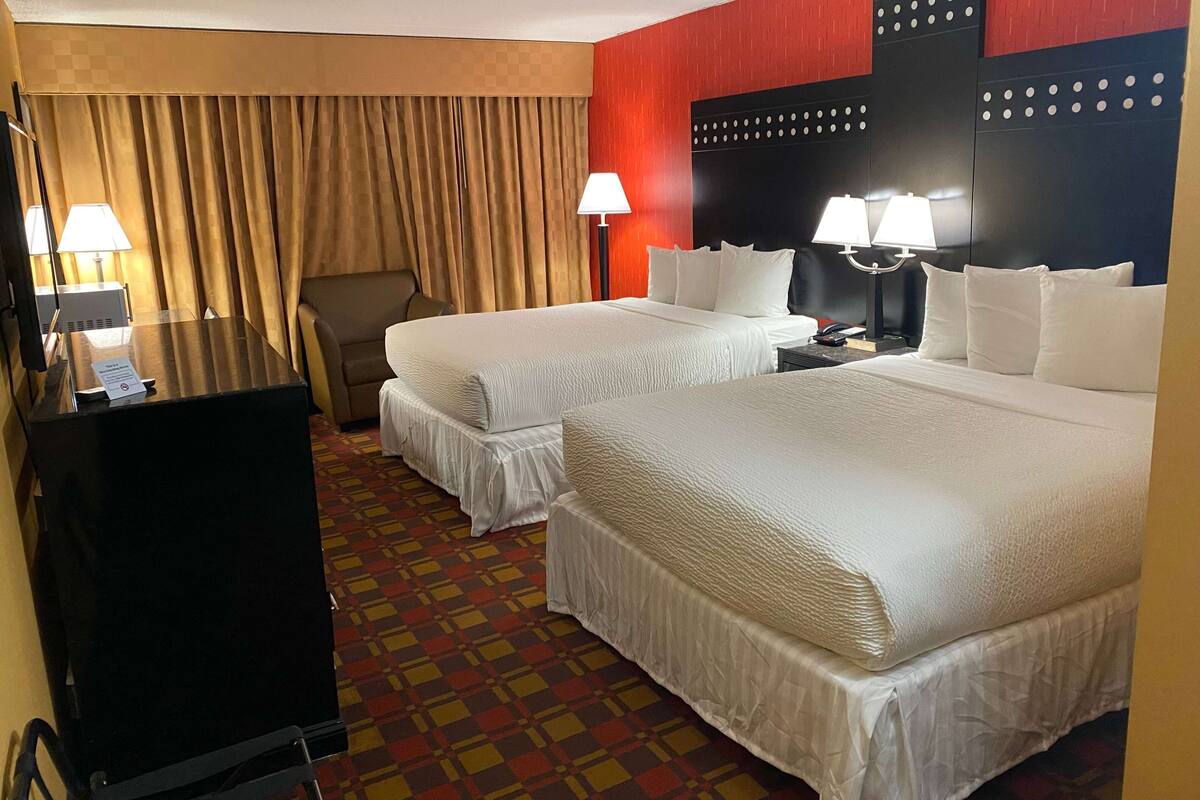 A hotel room with two beds, a desk, a chair, and a television.