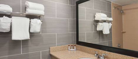 Un baño moderno con lavamanos de granito, un espejo grande y toallas blancas dobladas en un perchero.