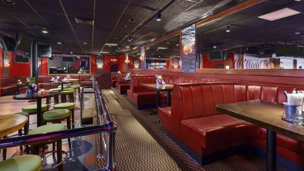 A restaurant with red booths and tables, a patterned carpet, and a modern ceiling design. - Ramada by Wyndham Rochelle Park Near Paramus (Rochelle Park)