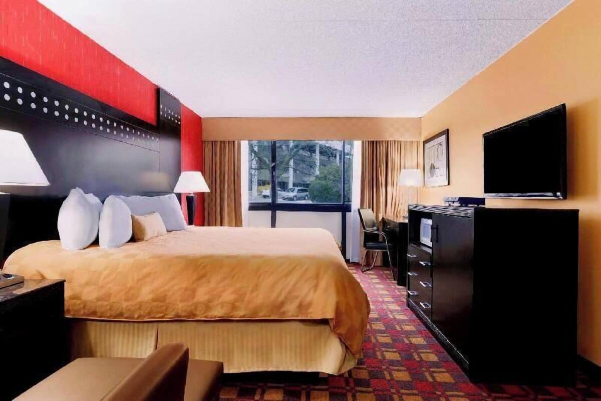 A hotel room with a bed, a desk, a television, and a window with a view of the outside.