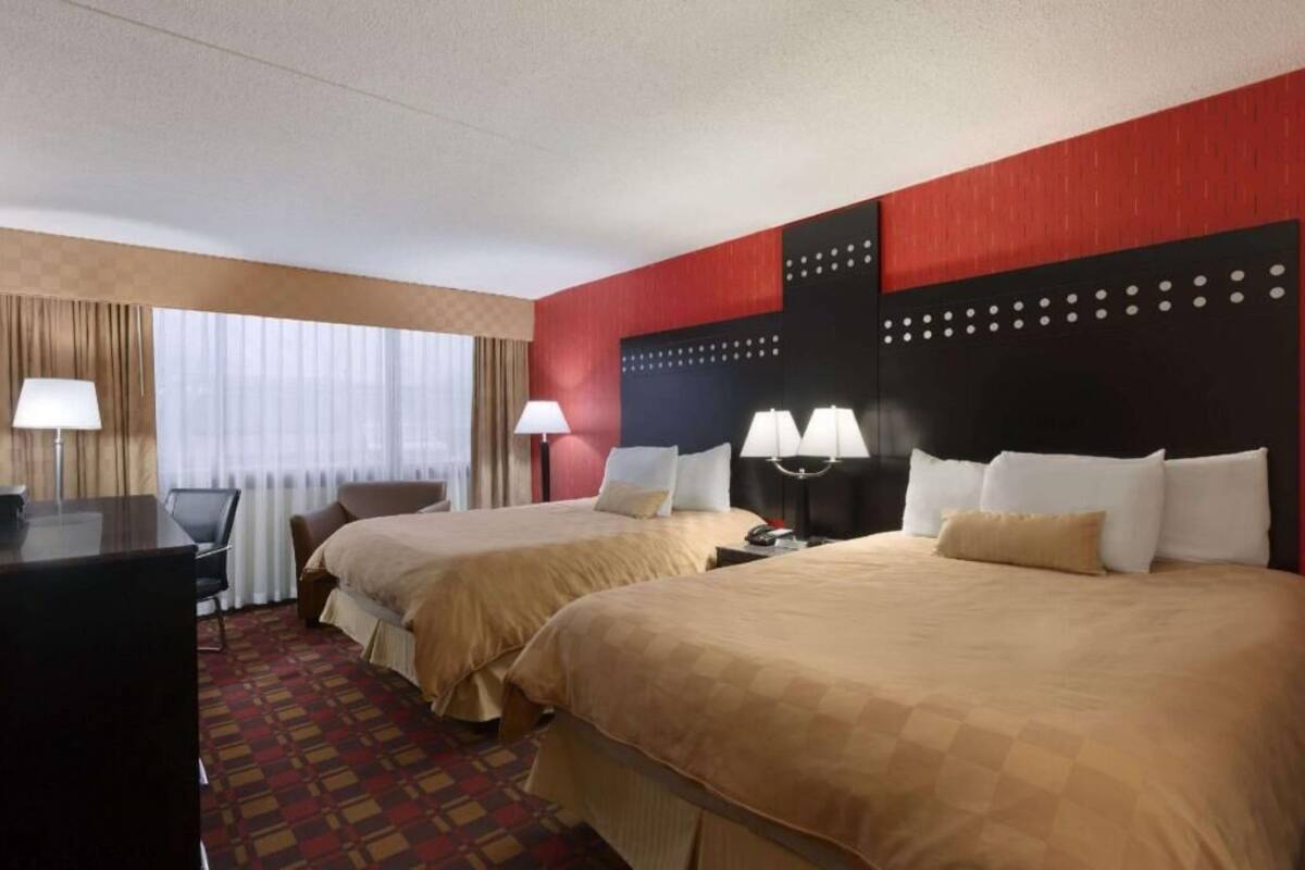 A hotel room with two beds, a desk, a chair, and a window with curtains.
