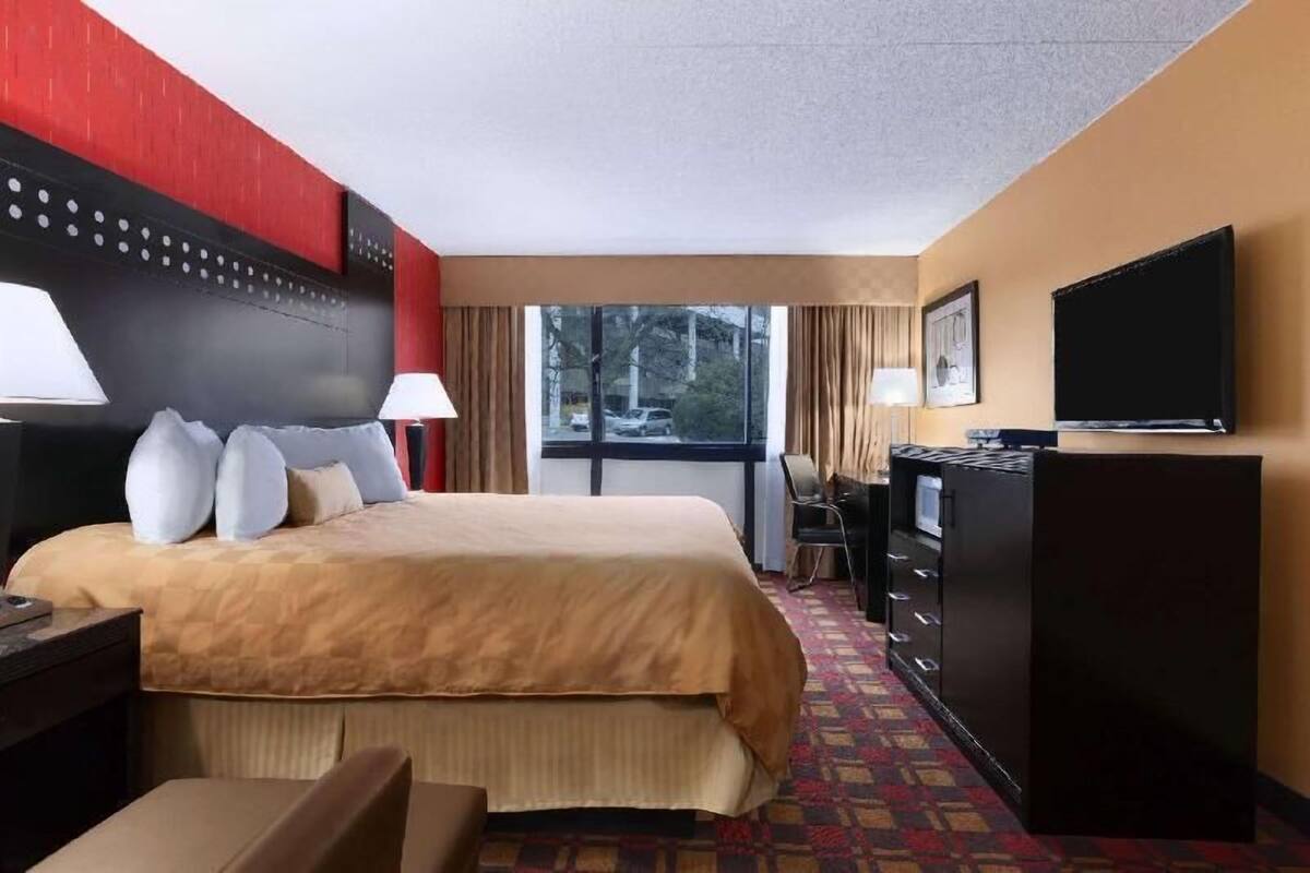A hotel room with a bed, a desk, a television, and a window with a view of the outside.