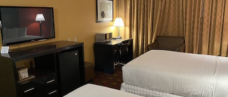 A hotel room with two beds, a desk with a computer, a television, and a lamp.