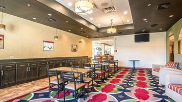 A hotel lobby with multiple tables and chairs, a patterned carpet, and a television mounted on the wall.