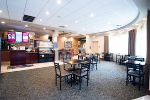 A restaurant with multiple tables and chairs, a counter with a menu display, and a ceiling with recessed lighting.
