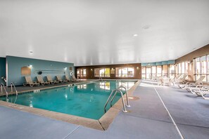 An indoor swimming pool with clear water, surrounded by lounge chairs and a tiled floor.