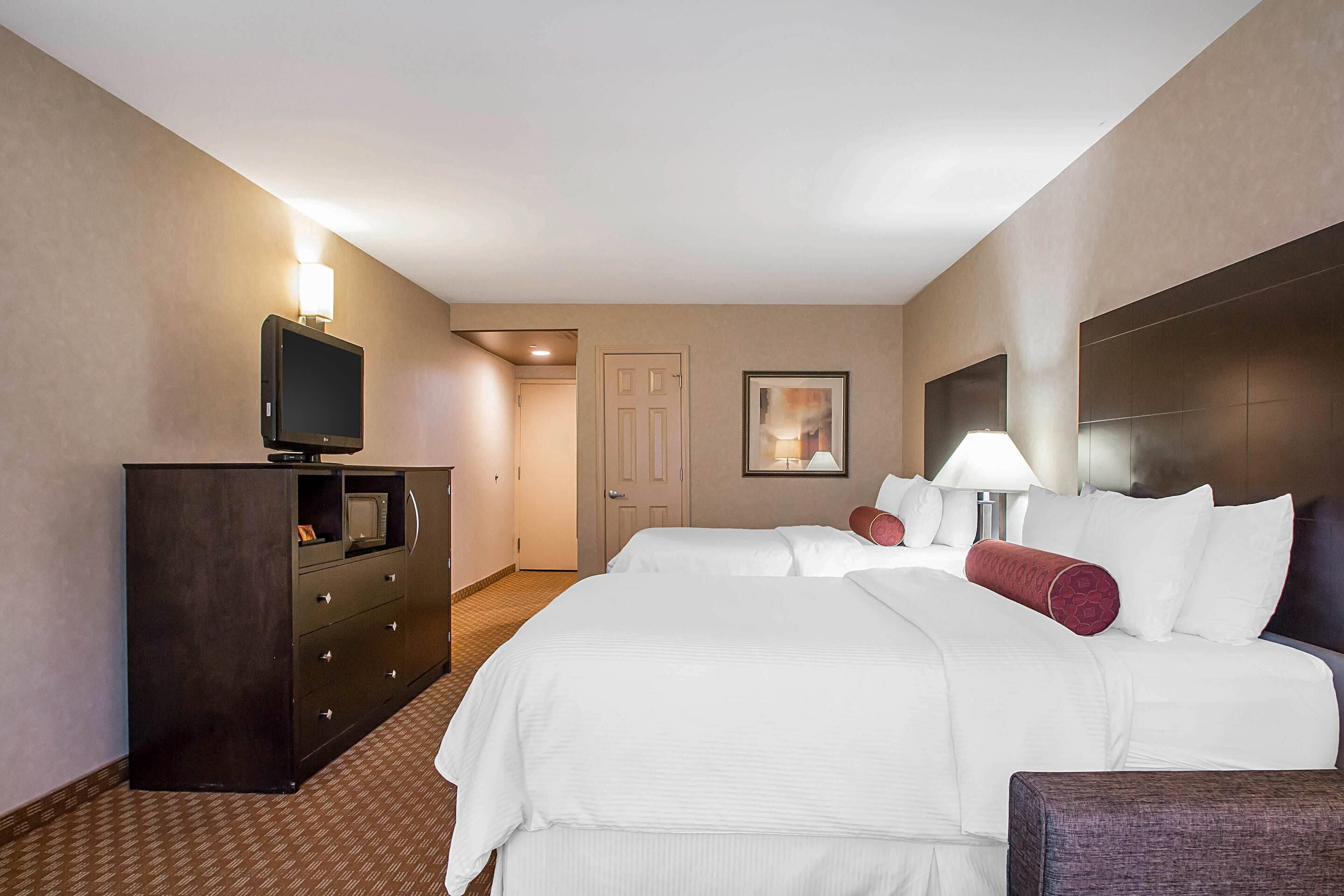 Une chambre d’hôtel avec un grand lit, une commode, une télévision et une porte donnant sur une autre pièce.