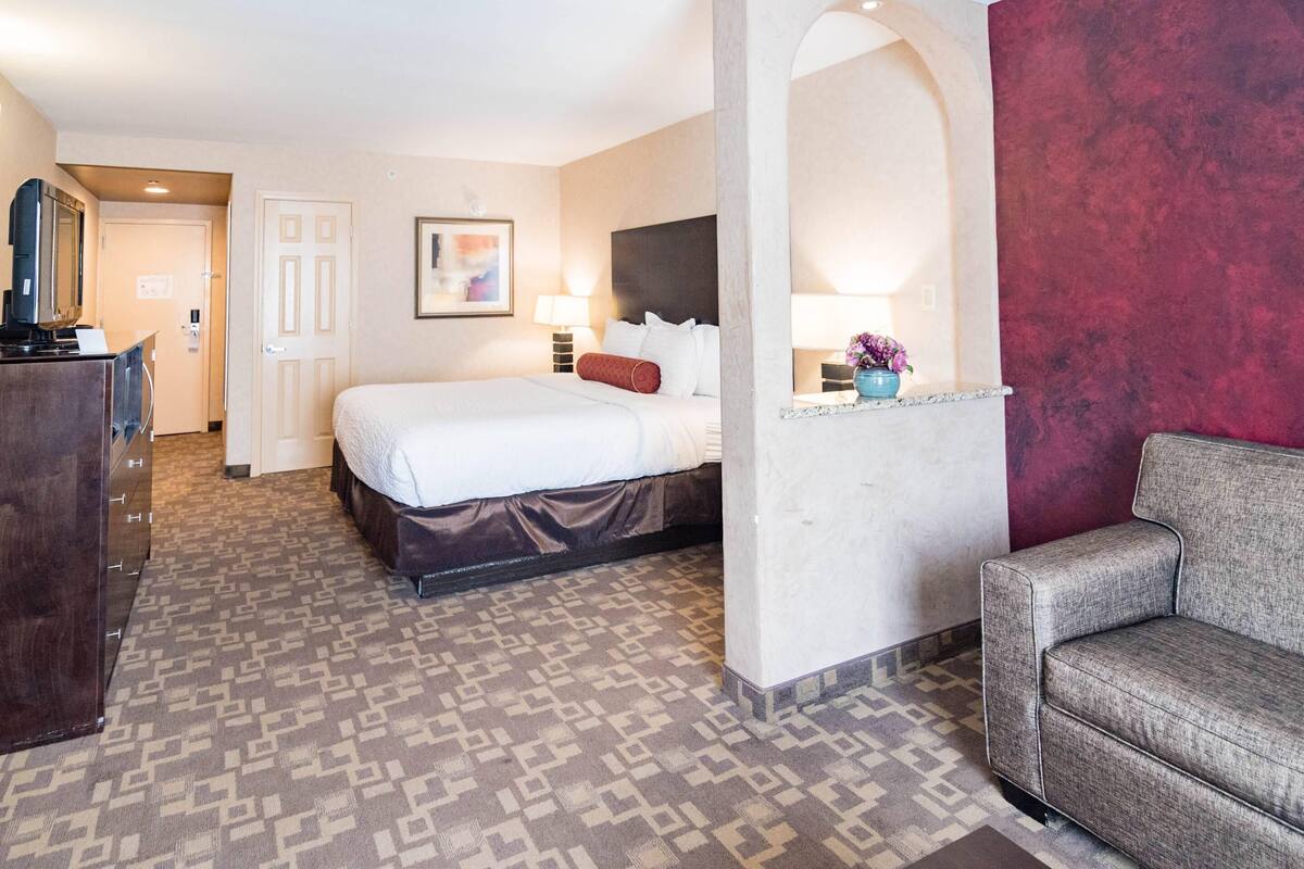 A hotel room with a bed, a dresser, a sofa, and a wall-mounted TV.