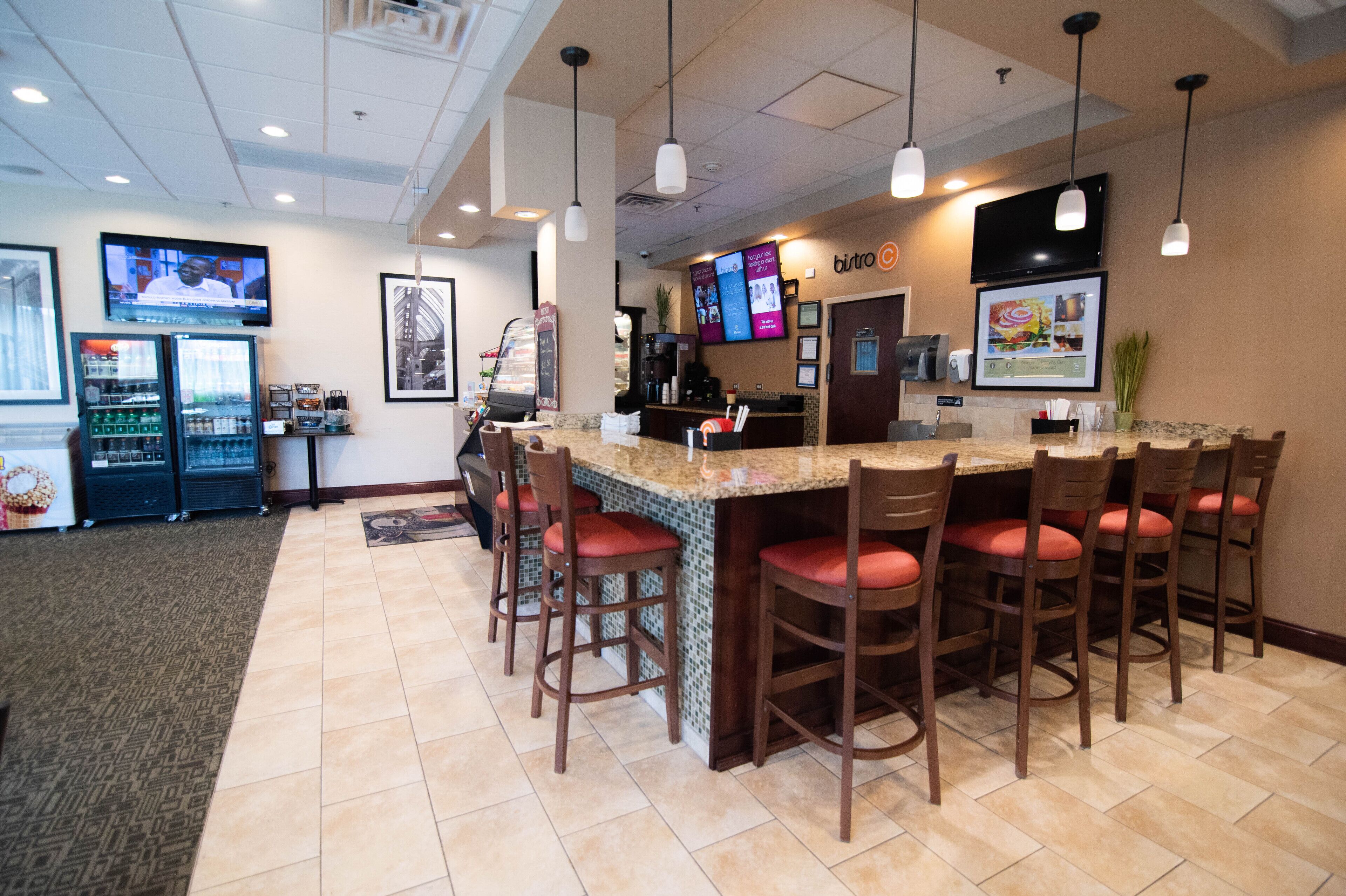 A bar area with a counter, multiple bar stools, a television mounted on the wall, and a coffee machine.