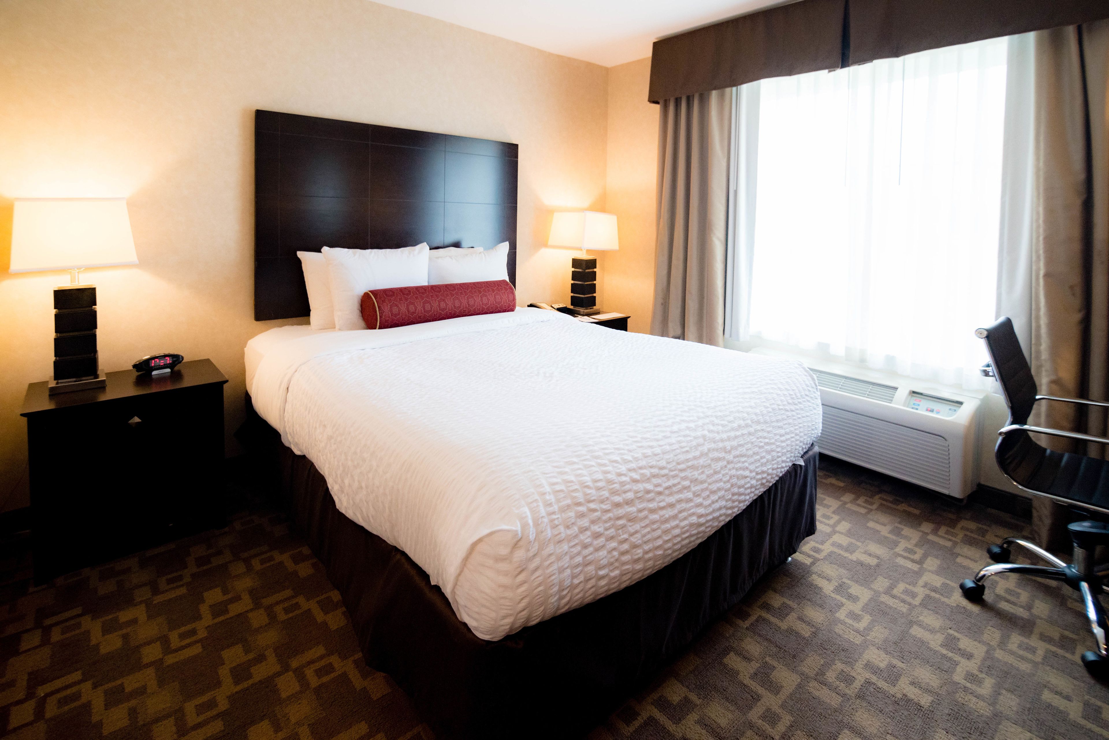 A hotel room with a large bed, two bedside tables with lamps, a chair, and a window with curtains.