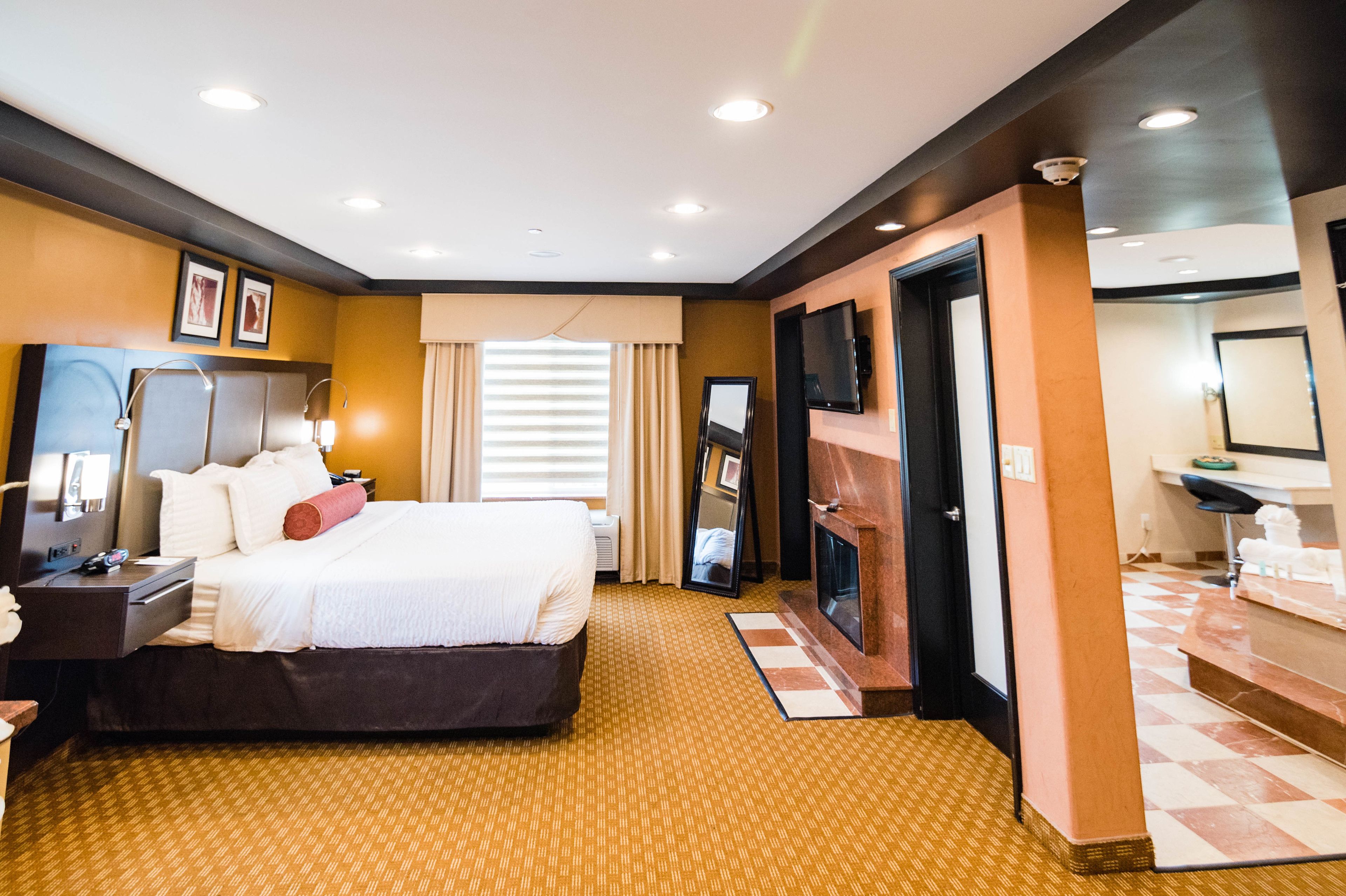 Ein Hotelzimmer mit einem großen Bett, Nachttischen, einem Fernseher, einem Spiegel und einem Kamin.
