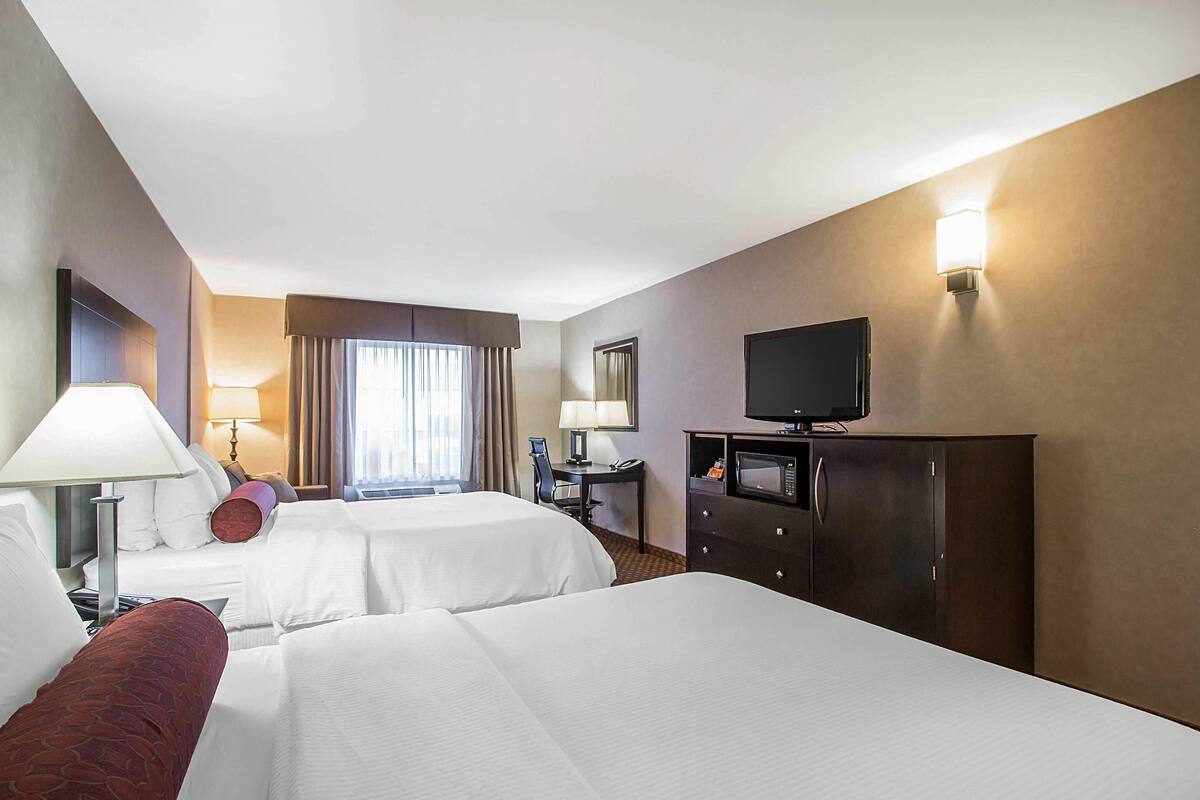 A hotel room with two beds, a desk, a TV, and a minibar.